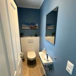 Badezimmer mit Toilette, Waschbecken und Spiegel an blauen Wänden.