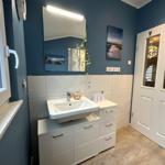Badezimmer mit Waschbecken, Spiegel und Fenster. Wandfarbe blau, Boden hell.