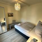 Schlafzimmer mit Bett, Kleiderschrank und Hängespiegel. Deckenleuchte und Holzboden.