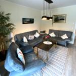Wohnzimmer mit zwei Sofas, Sessel, Couchtisch und Pflanze. Küche im Hintergrund sichtbar.