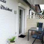 Haus Windsbraut mit Terrasse, Tisch, Stühlen und Pflanzen an der weißen Wand.