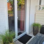 Terrasse mit Glastür, Pflanzen und Bodenmatte. Blick auf Garten und Nachbarhaus.