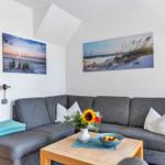 Grauer Sofa mit weißen Kissen, Holztisch, Wandbilder und Stehlampe.