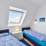 Zwei Einzelbetten mit blauer Bettwäsche, Dachfenster und Wandlampen.