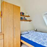 Schlafzimmer mit Dachschräge, Bett, Kleiderschrank und Dachfenster.