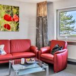 Wohnzimmer mit rotem Sofa, Sessel und Glas-Tisch. Fenster mit Blick auf Bäume.