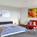 Schlafzimmer mit Bett, rotem Sofa und Wandbildern