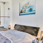 Schlafzimmer mit Bett, Nachttisch und Wandbild mit Fahrrad.