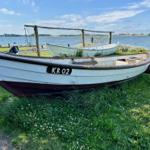 Weißes Boot mit Kennzeichnung KR 02 steht auf Gras am Wasser.