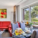 Ein Wohn- und Essbereich mit rotem Sofa, Glas-Tisch und Blick auf Grün.