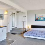 Schlafzimmer mit Bett, Küchenzeile und Wandbild mit Fahrrad.