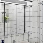 Badezimmer mit Spiegel, Waschbecken und weißen Fliesen.