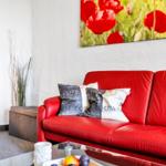 Rotes Sofa mit Kissen, Glas-Tisch und Wandbild mit Mohnblumen.