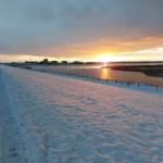 Schneebedeckter Weg entlang eines gefrorenen Sees bei Sonnenuntergang.