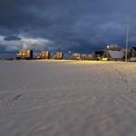 Schneebedeckter Platz mit beleuchteten Häusern unter bewölktem Himmel.
