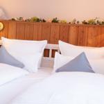 Doppelbett mit weißen Bettwäsche und grauen Kissen. Holzpaneelen und Wandlampen.