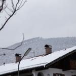 Schneebedecktes Dach mit Schornsteinen und verschneiten Bergen im Hintergrund.