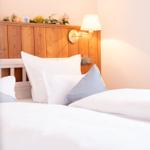 Doppelbett mit weißer Bettwäsche und Holzkopfteil. Wandlampe und Blumen dekorieren den Raum.