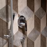 Dusche mit Chromarmatur und geometrischem Fliesenmuster in Braun- und Grautönen.
