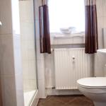 Badezimmer mit Dusche, Toilette und Waschbecken. Fenster mit Handtuchstapel.