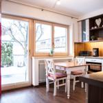 Essbereich mit Tisch, Stühlen und Küchenzeile. Fenster mit roten Vorhängen. Draußen Schnee.