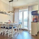 Dining area with table, chairs, and view to balcony. Kitchen with microwave and sink.