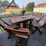 Terrace with wooden table and chairs, flowers, and view of houses.