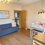 Living and dining area with sofa, table and chairs. Wooden floor and staircase visible.