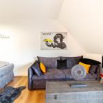 Schlafzimmer mit Sofa, Kamin und Wandbild. Bett links, Holzboden.