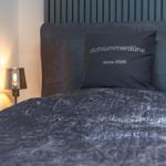 Bettkopfteil mit Kissen, auf dem Schlummerdüne since 2026 steht, und Nachttischlampe.