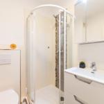 Badezimmer mit Dusche, Waschbecken und Toilette. Weiße Fliesen und Spiegelschrank.