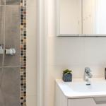 Badezimmer mit Dusche und Waschbecken. Mosaikfliesen an der Duschwand.