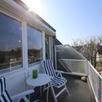 Terrasse mit zwei Stühlen und Tisch, weißer Geländer und Glaswand.