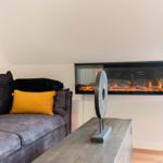 Ein Wohnzimmer mit grauem Sofa, gelbem Kissen und integriertem Kamin.