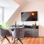 Dining area with round table, four chairs, TV, and large window.