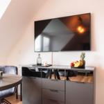 TV an der Wand, Schrank mit Obst und Flasche, Sitzgelegenheit im Dachgeschoss.