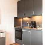 Küche mit dunklen Schränken, Herd und Spüle. Fernseher und Obst auf Sideboard.