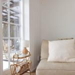 Ein Sofa mit Kissen steht neben einem Fenster mit Rattanbeistelltisch.