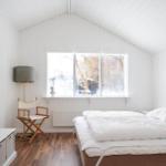 Schlafzimmer mit weißem Bett, Holzboden und großem Fenster.