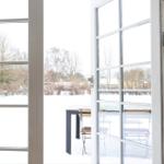 Durch offene Tür blickt man auf verschneiten Garten mit Tisch und Stühlen.