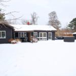Schwarzes Haus mit Schneebedecktem Dach und Gartenmöbeln im Winter.