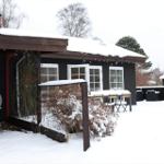 Schwarzes Haus mit Schnee, weißen Fenstern und Gartenmöbeln.