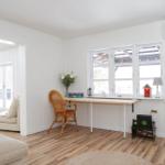 Ein Arbeitsbereich mit Schreibtisch, Stuhl und Fenster. Holzboden und weiße Wände.