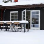 Schneebedeckter Außenbereich mit Tisch und Stühlen vor einem Haus mit weißen Fenstern.