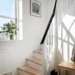 Staircase with wooden steps, black handrail, and window with plant.