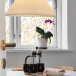 Table with coffee maker, mugs, and plant by window