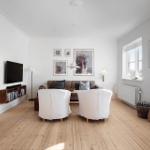 Living room with wooden floor, sofa, two white chairs, and wall art.