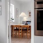 Dining area with wooden table, chairs, and window. Kitchen with stainless steel appliances.