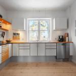 Kitchen with wooden floor, white cabinets, and window with view of trees.