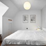 Bedroom with sloped ceiling, bed, lamp, and wall art.